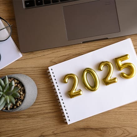 2025 represented in gold lettering on a notebook with a pen, plant and laptop beside it
