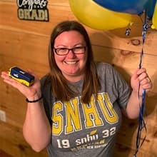 Laura Gaughan wearing an SNHU shirt, holding a miniature SNHU bus and balloons.
